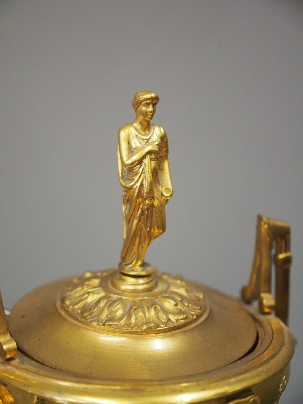A white marble mantel clock featuring gilt bronze mounts, winged griffin corner supports, and a classical urn finial topped with a standing figure. View IV