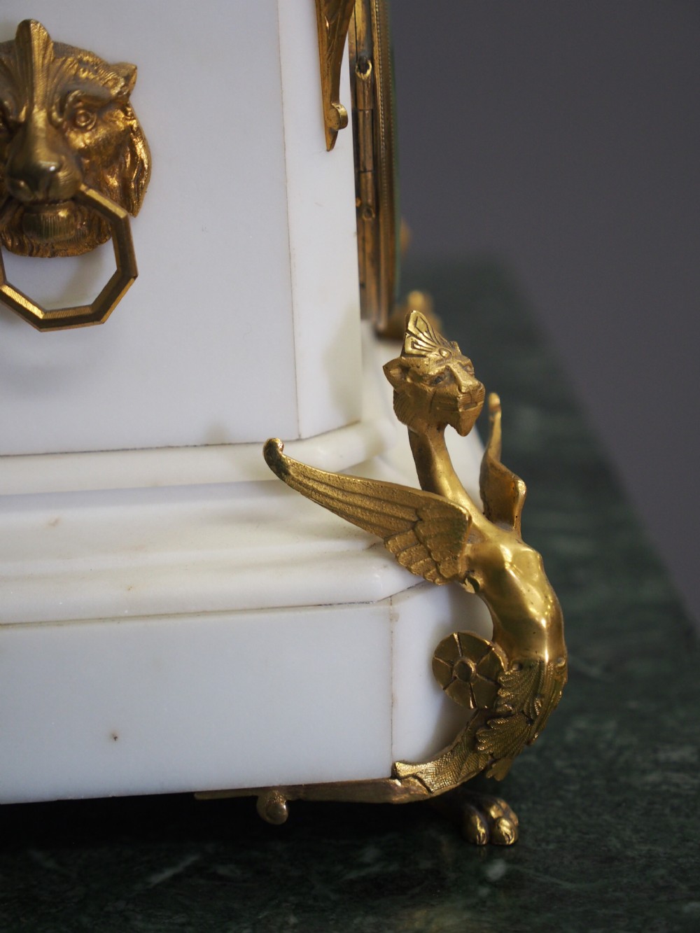 A white marble mantel clock featuring gilt bronze mounts, winged griffin corner supports, and a classical urn finial topped with a standing figure. View XI