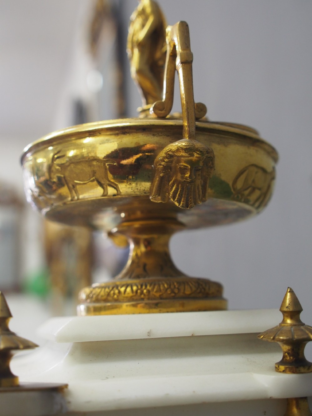 A white marble mantel clock featuring gilt bronze mounts, winged griffin corner supports, and a classical urn finial topped with a standing figure. View XII
