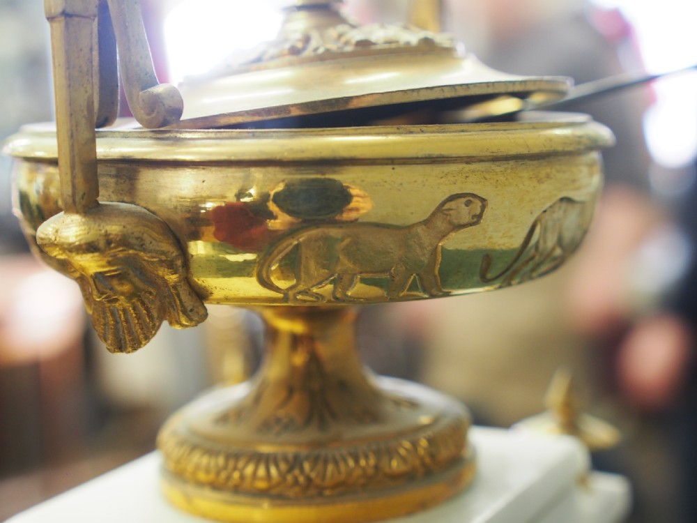 A white marble mantel clock featuring gilt bronze mounts, winged griffin corner supports, and a classical urn finial topped with a standing figure. View XIV