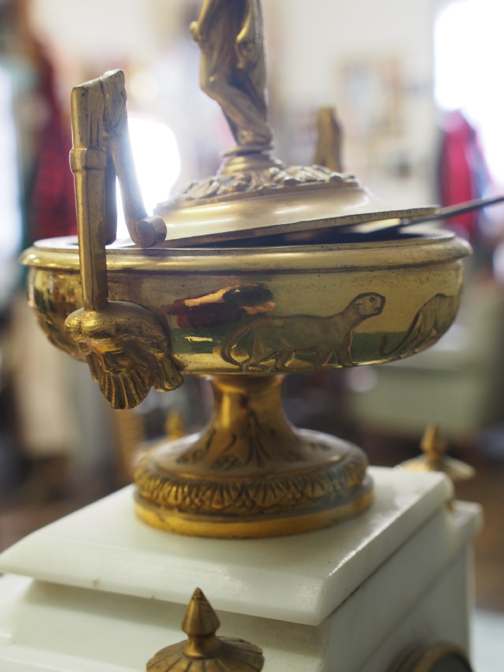 A white marble mantel clock featuring gilt bronze mounts, winged griffin corner supports, and a classical urn finial topped with a standing figure. View XV