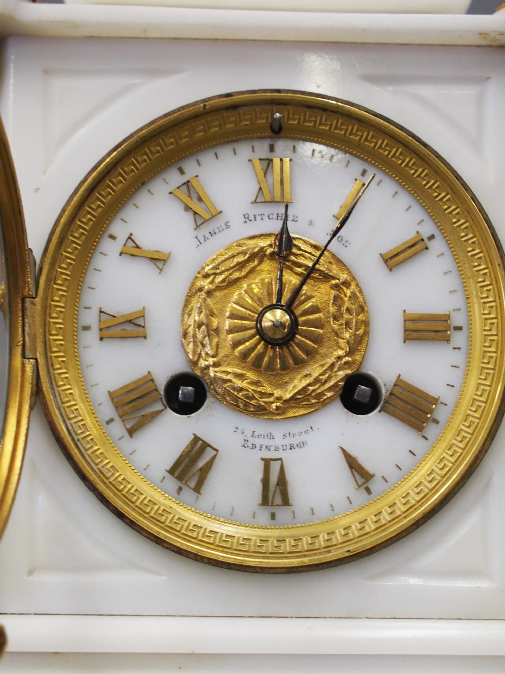 A white marble mantel clock featuring gilt bronze mounts, winged griffin corner supports, and a classical urn finial topped with a standing figure. View XVII