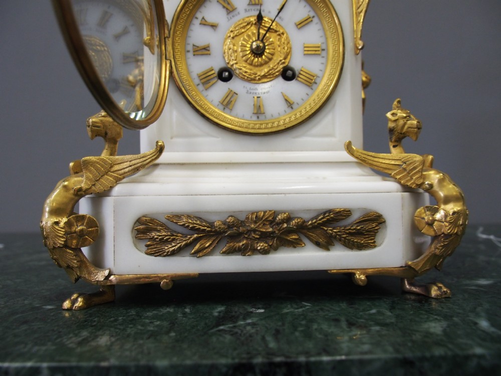 A white marble mantel clock featuring gilt bronze mounts, winged griffin corner supports, and a classical urn finial topped with a standing figure. View XVIII