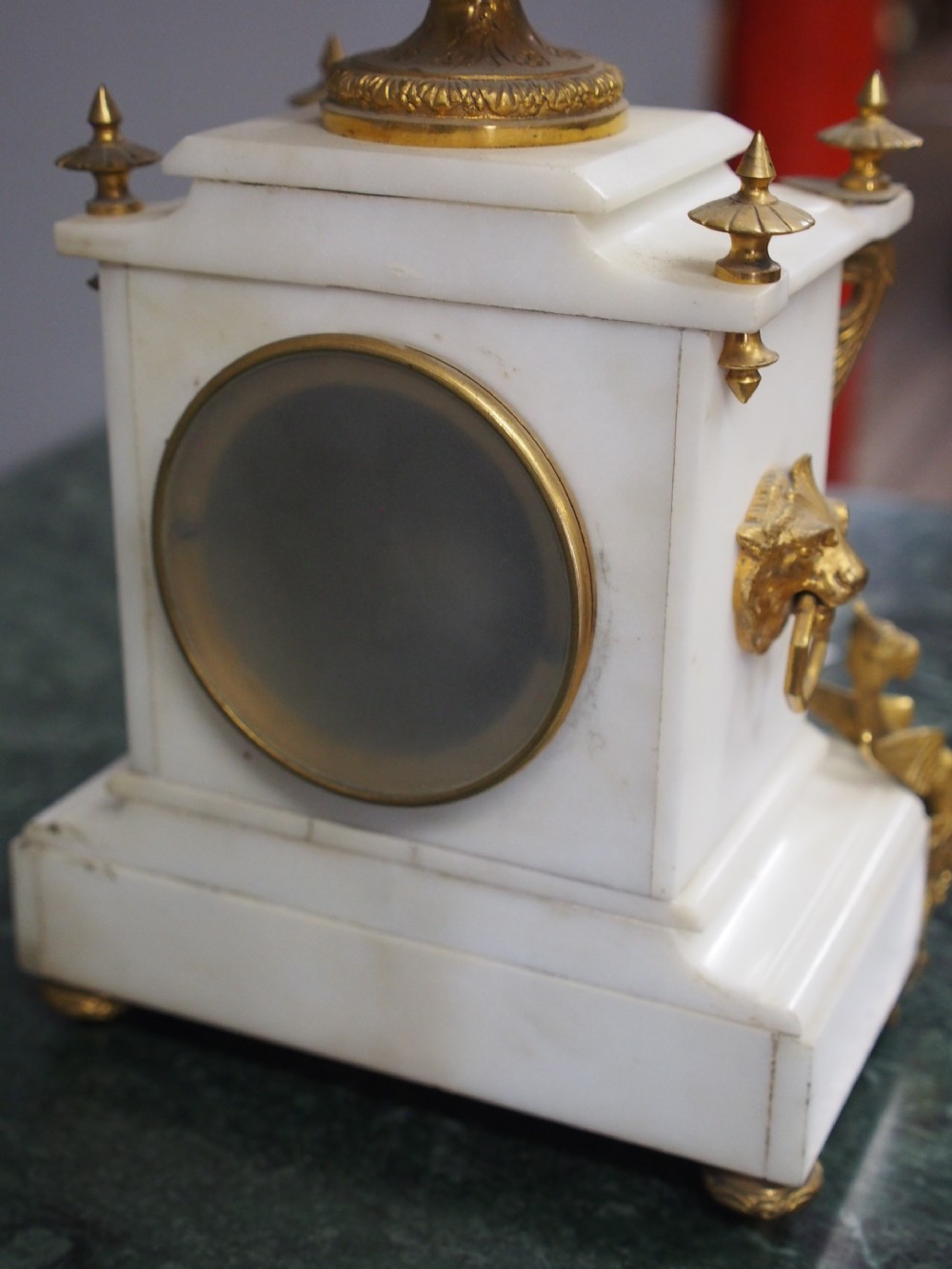 A white marble mantel clock featuring gilt bronze mounts, winged griffin corner supports, and a classical urn finial topped with a standing figure. View XX
