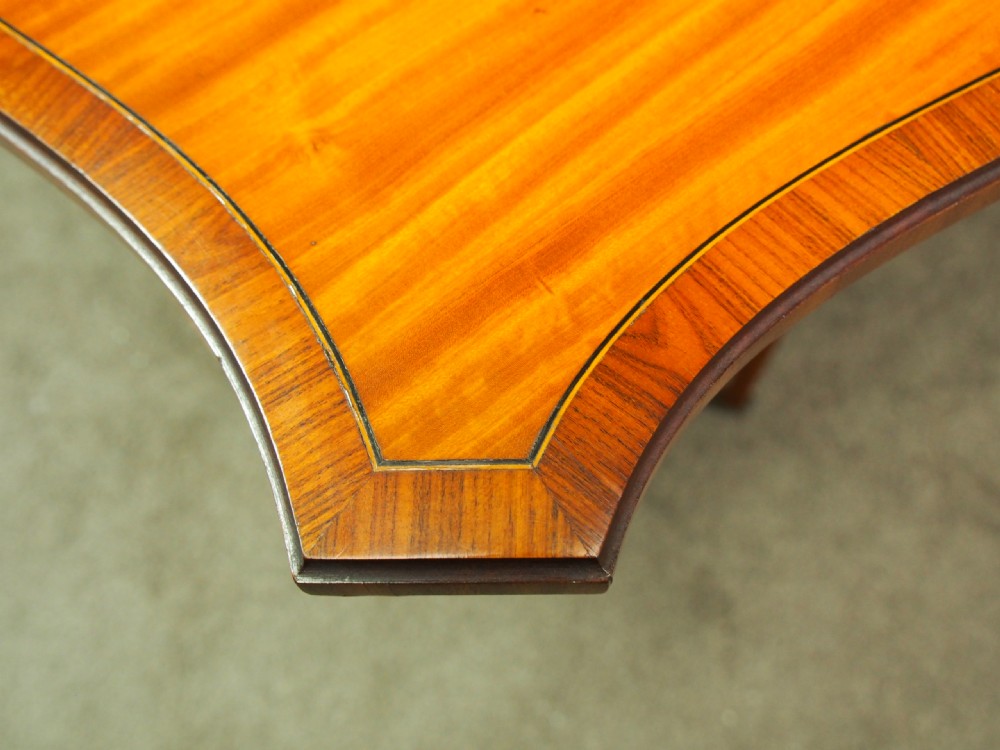 An Edwardian satinwood Sutherland table shown folded with curved drop-leaf sides, fretwork side supports, and brass castors. View V