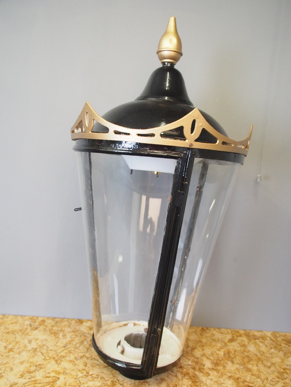 A tapered circular street lamp lantern featuring a black domed cap with a gold finial, gold filigree trim, and clear glass side panels. View III