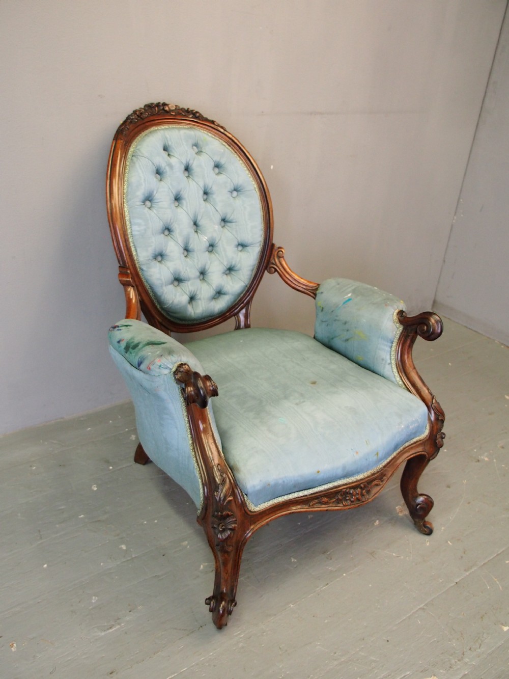 A Victorian carved walnut armchair featuring light blue button-tufted backrest upholstery, padded armrests, cabriole front legs, and metal castors. View II