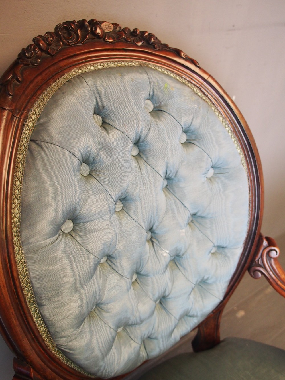 A Victorian carved walnut armchair featuring light blue button-tufted backrest upholstery, padded armrests, cabriole front legs, and metal castors. View III