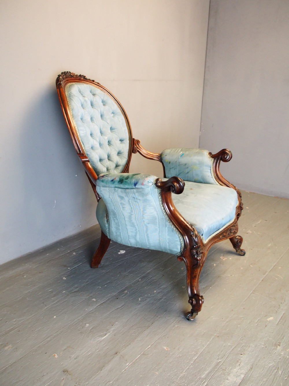 A Victorian carved walnut armchair featuring light blue button-tufted backrest upholstery, padded armrests, cabriole front legs, and metal castors. View IV