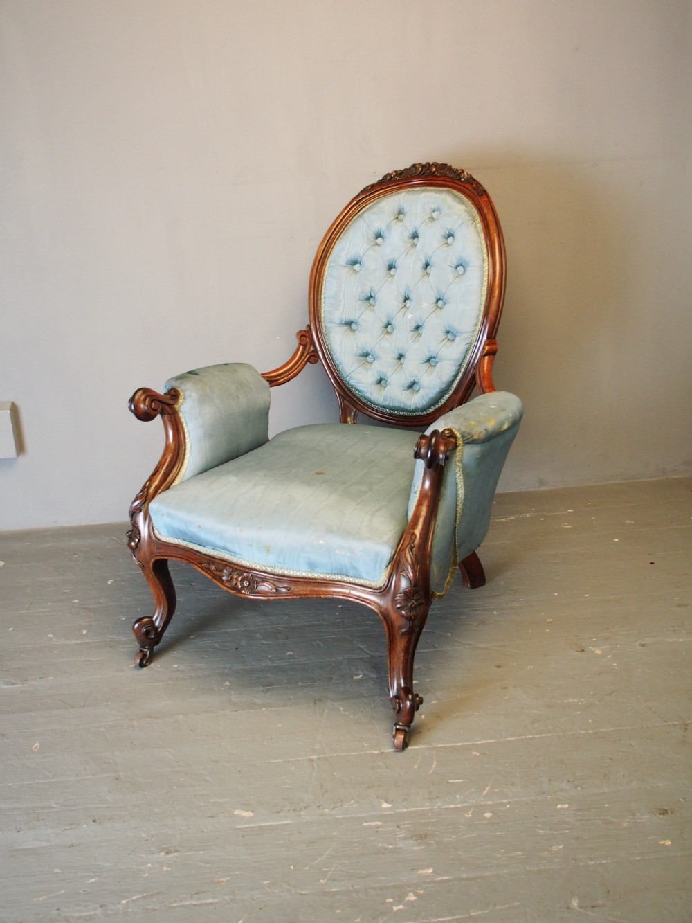 A Victorian carved walnut armchair featuring light blue button-tufted backrest upholstery, padded armrests, cabriole front legs, and metal castors. View V