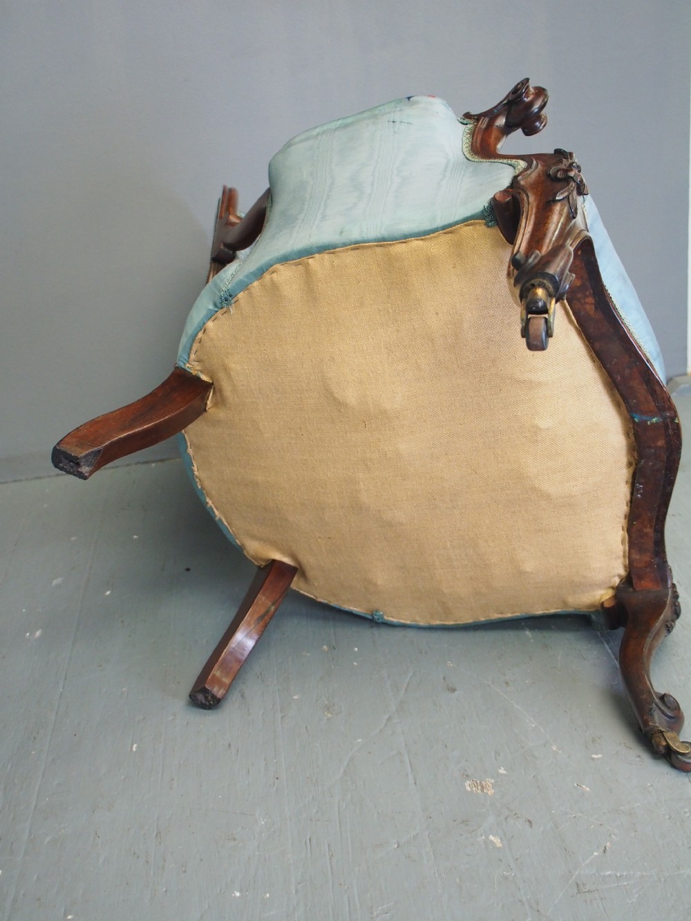 A Victorian carved walnut armchair featuring light blue button-tufted backrest upholstery, padded armrests, cabriole front legs, and metal castors. View VI