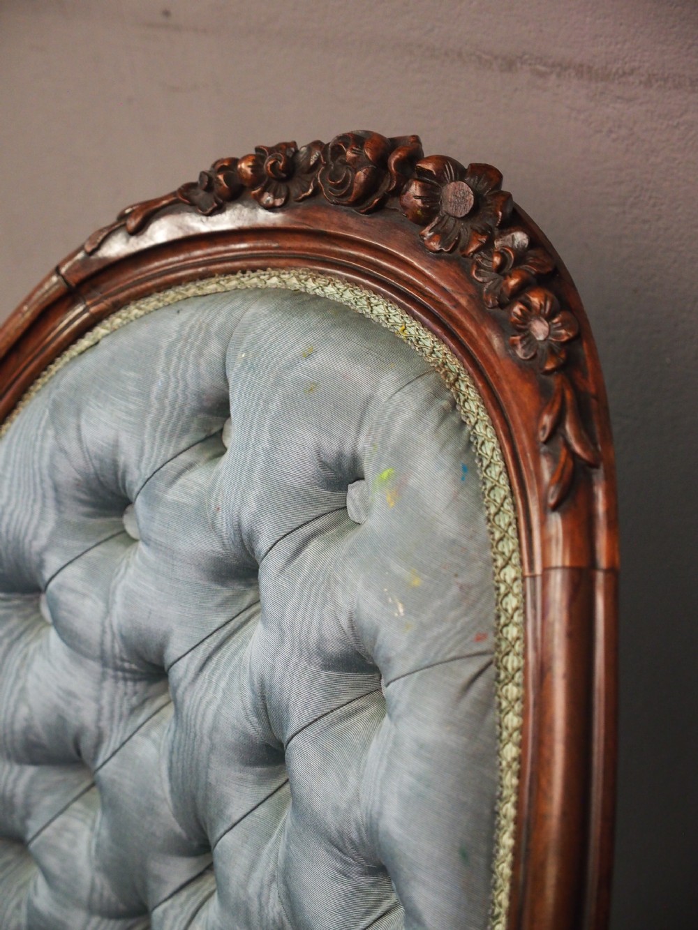 A Victorian carved walnut armchair featuring light blue button-tufted backrest upholstery, padded armrests, cabriole front legs, and metal castors. View XVIII