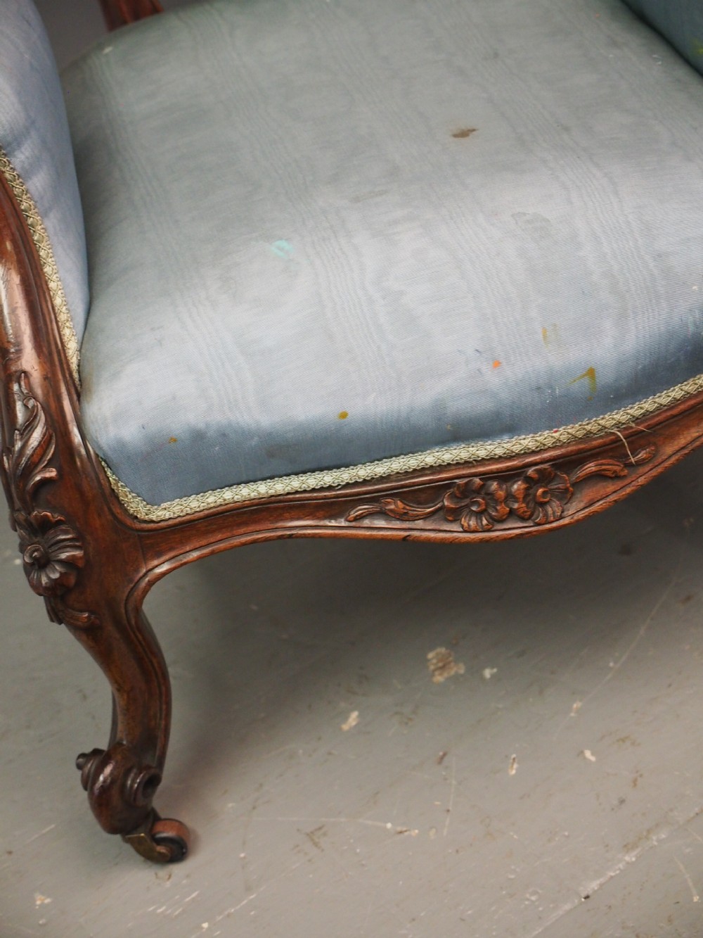 A Victorian carved walnut armchair featuring light blue button-tufted backrest upholstery, padded armrests, cabriole front legs, and metal castors. View XXI