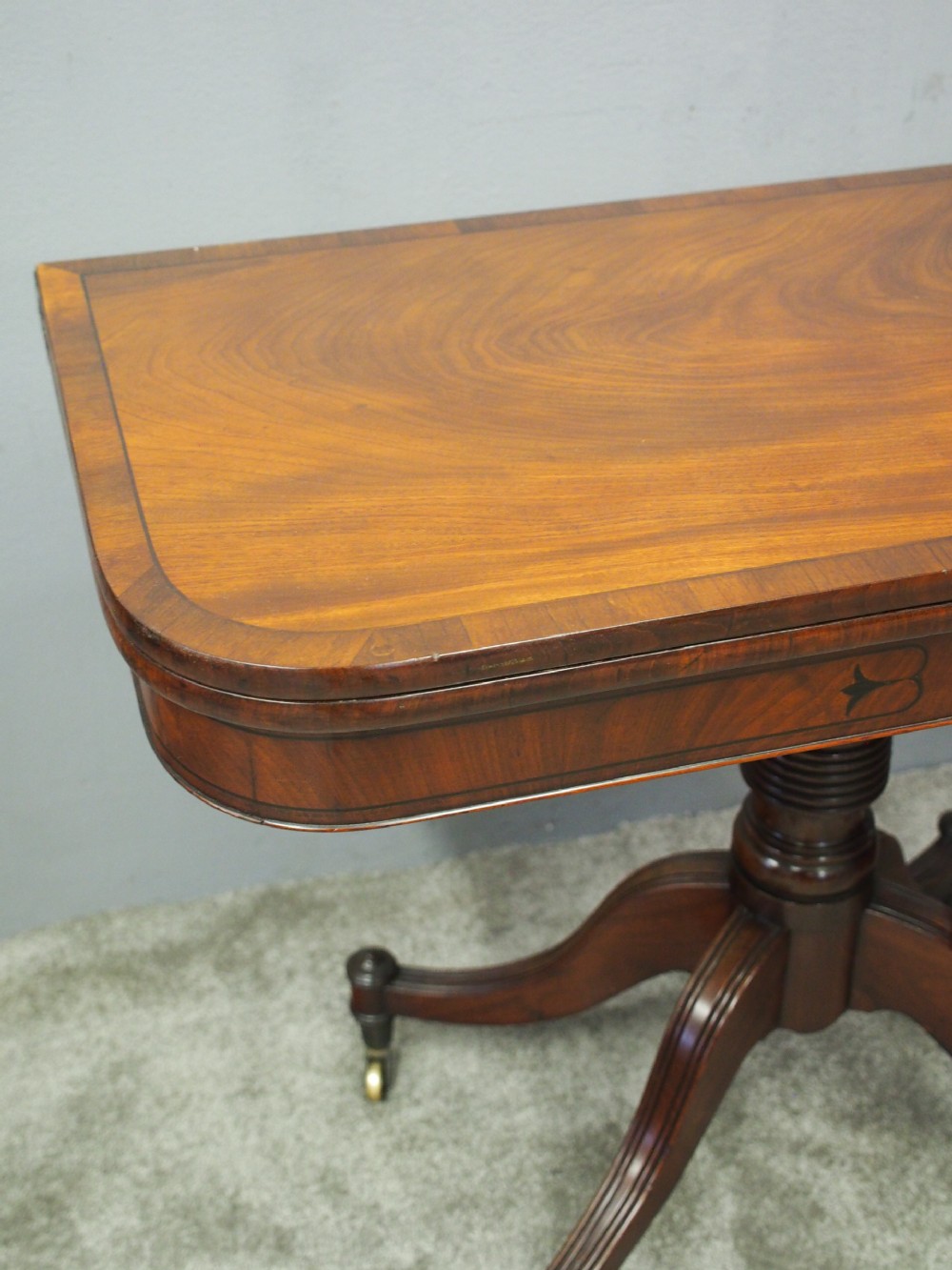 A Regency mahogany foldover card table featuring rosewood inlay along the apron, a turned central pedestal, and four swept legs with brass castors. View II