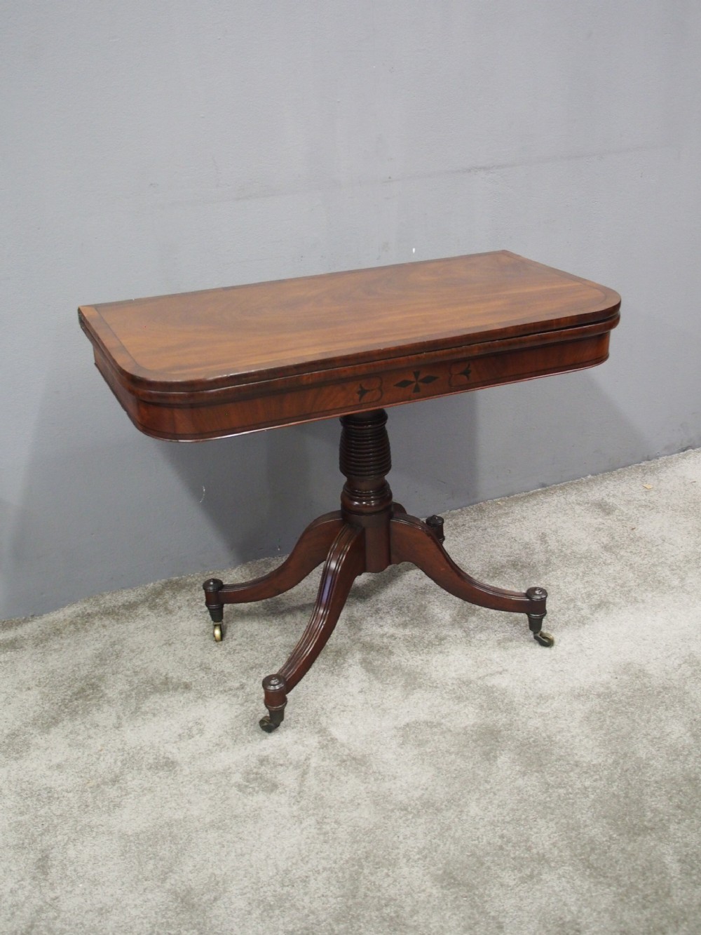 A Regency mahogany foldover card table featuring rosewood inlay along the apron, a turned central pedestal, and four swept legs with brass castors. View III
