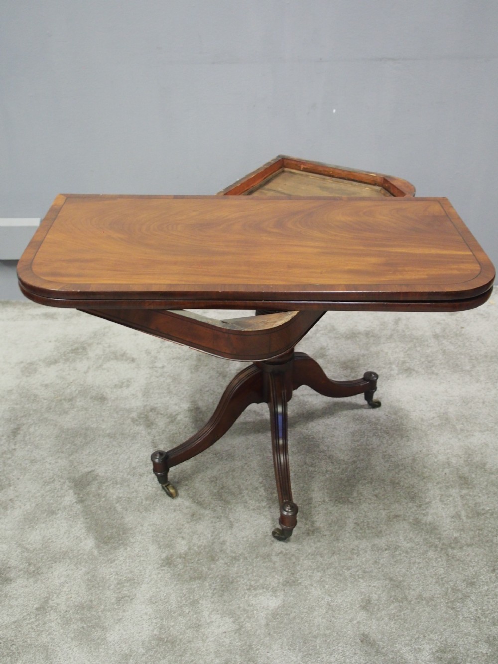 A Regency mahogany foldover card table featuring rosewood inlay along the apron, a turned central pedestal, and four swept legs with brass castors. View VI
