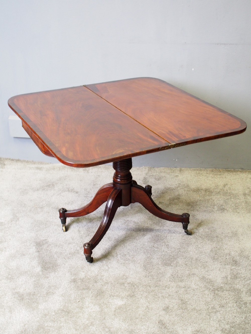 A Regency mahogany foldover card table featuring rosewood inlay along the apron, a turned central pedestal, and four swept legs with brass castors. View VIII