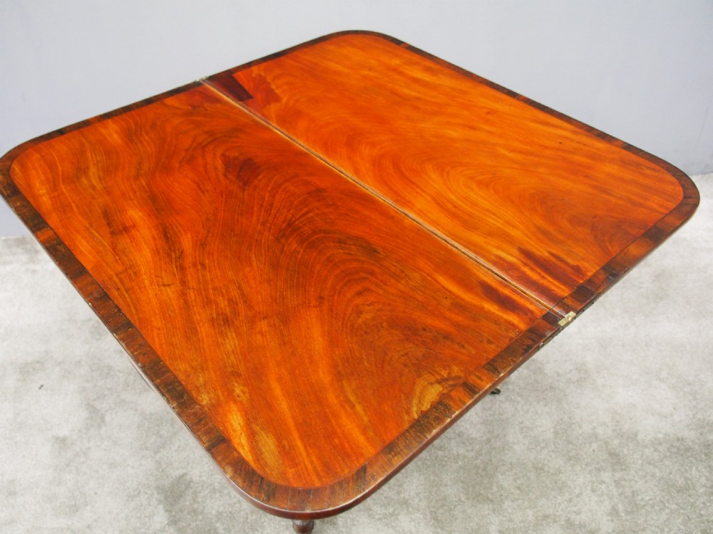 A Regency mahogany foldover card table featuring rosewood inlay along the apron, a turned central pedestal, and four swept legs with brass castors. View IX