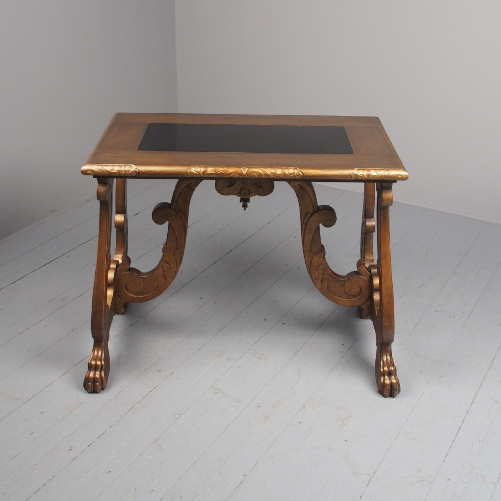 A Spanish style gilded side table featuring carved scroll legs with paw feet, a central drop pendant, and a dark leather inset top.
