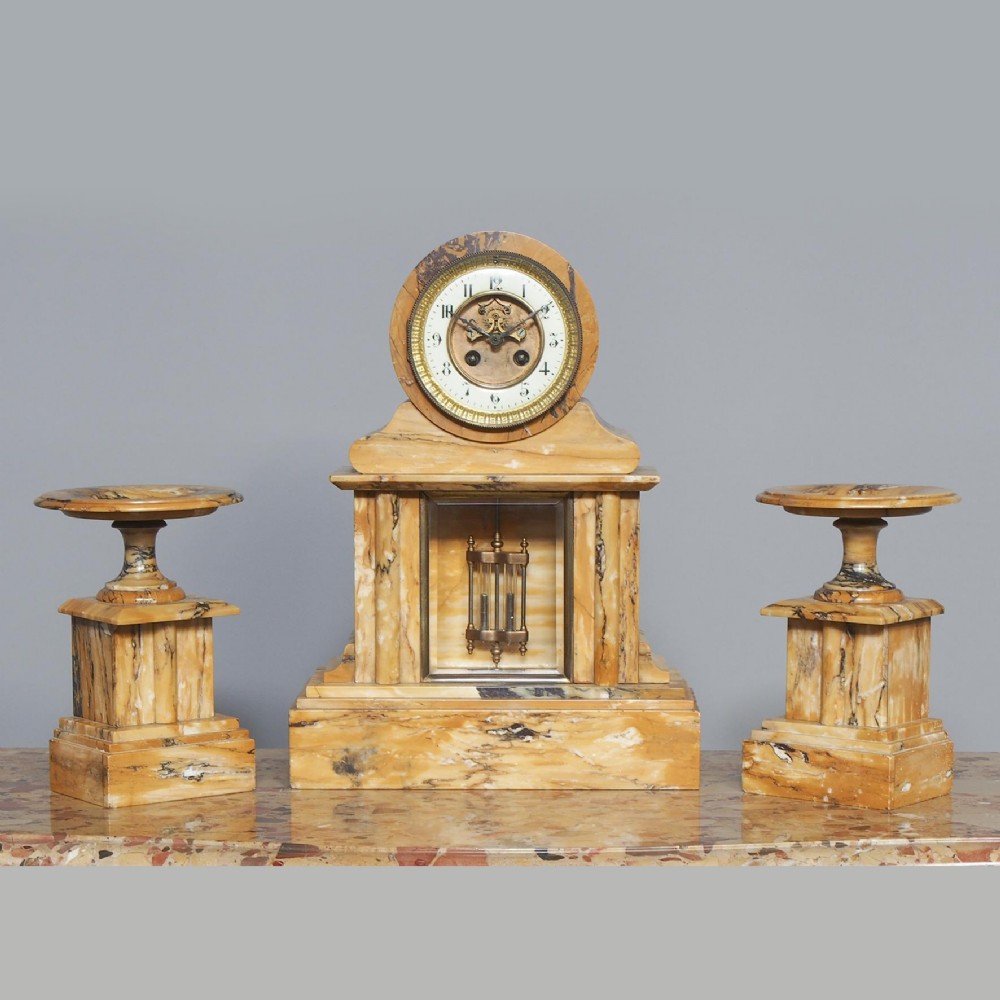 A three-piece sienna marble clock garniture featuring an architectural central clock with a visible pendulum flanked by two matching pedestal tazzas.