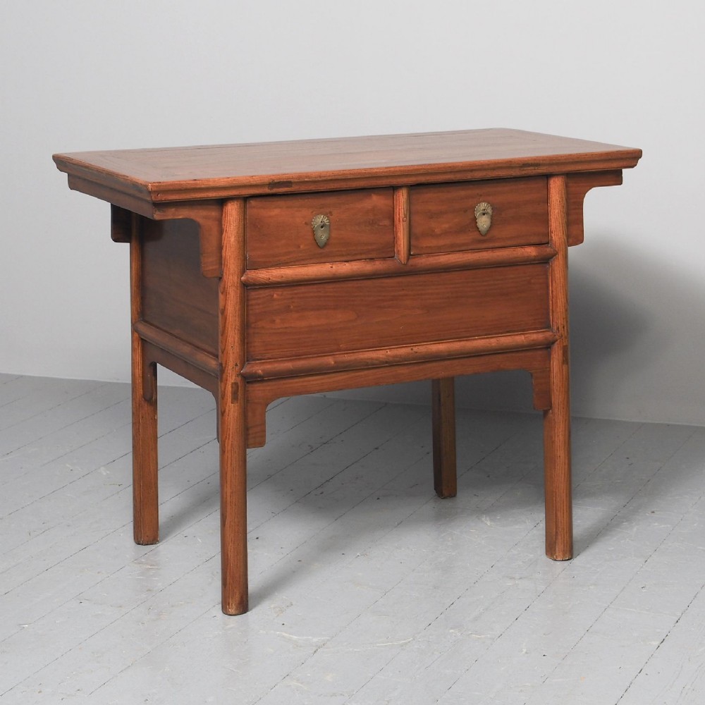 A warm brown Chinese elm altar table with an overhanging top, two brass-fitted drawers, and straight carved legs.