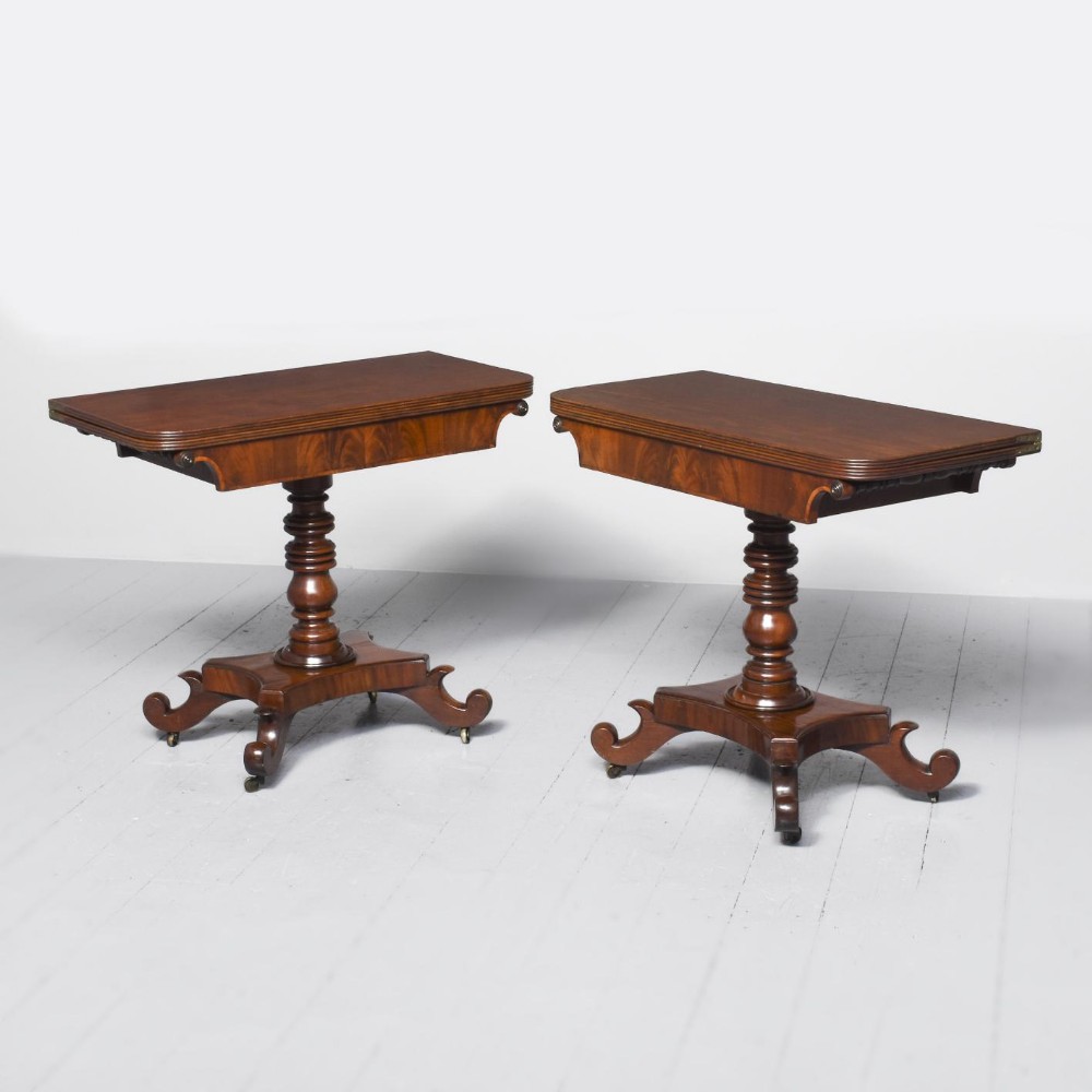 A pair of George IV mahogany fold-over tea tables with turned pedestals and scroll legs on brass castors.