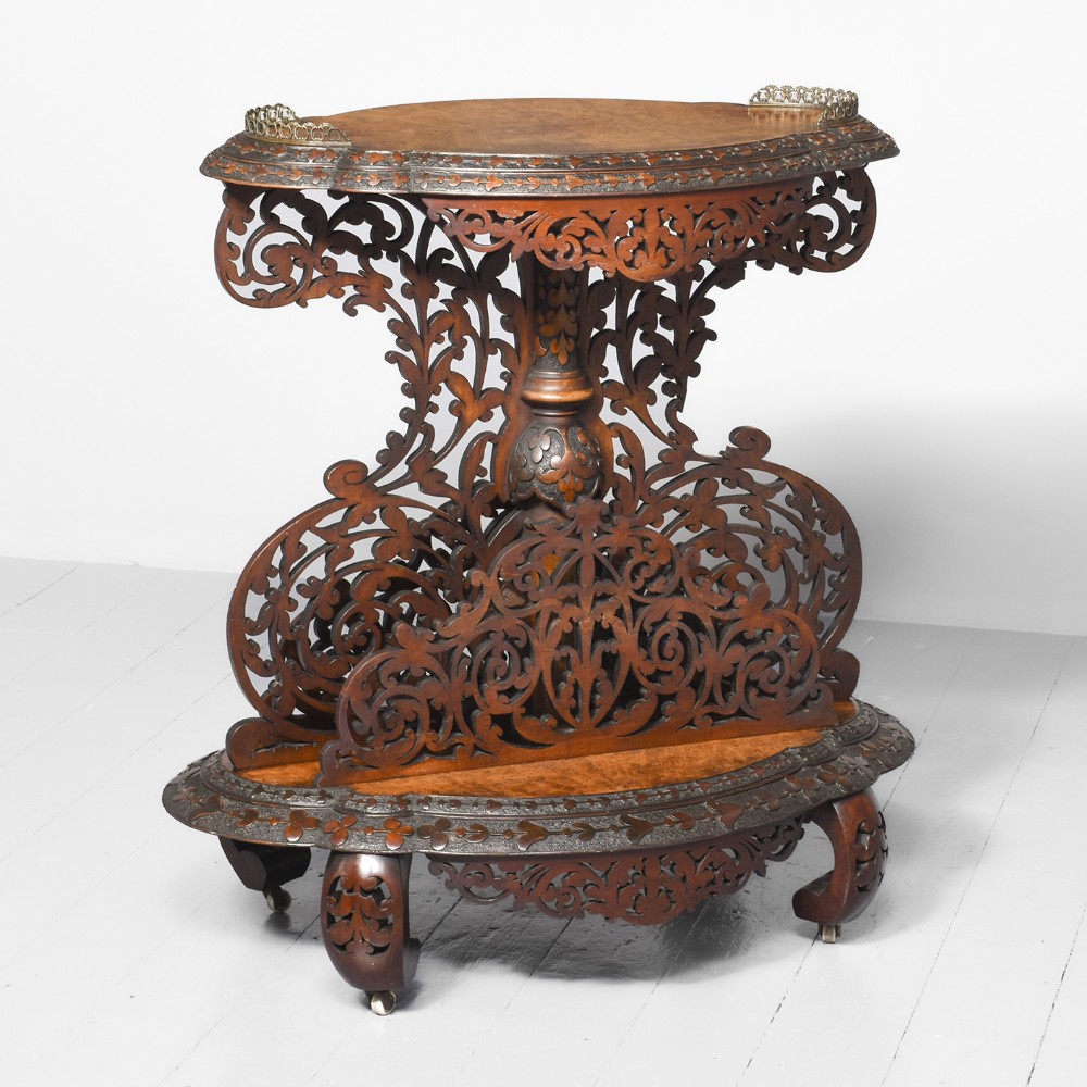 A Victorian carved walnut whatnot featuring intricate open fretwork panels, a lower divided shelf, turned support column, and an oval top with brass gallery corner trim.