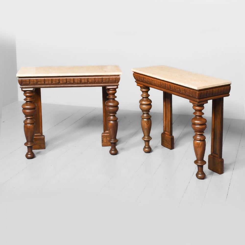 A pair of dark wood side tables featuring light beige marble tops, carved fluted aprons, and turned baluster legs.