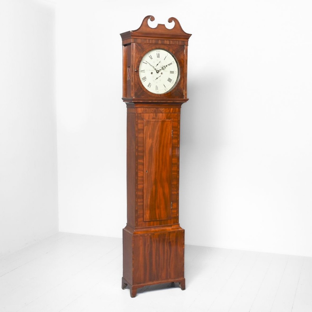 An antique Georgian mahogany longcase clock featuring a swan-neck pediment, a circular painted dial with Roman numerals, and a tall trunk with flame mahogany veneer.