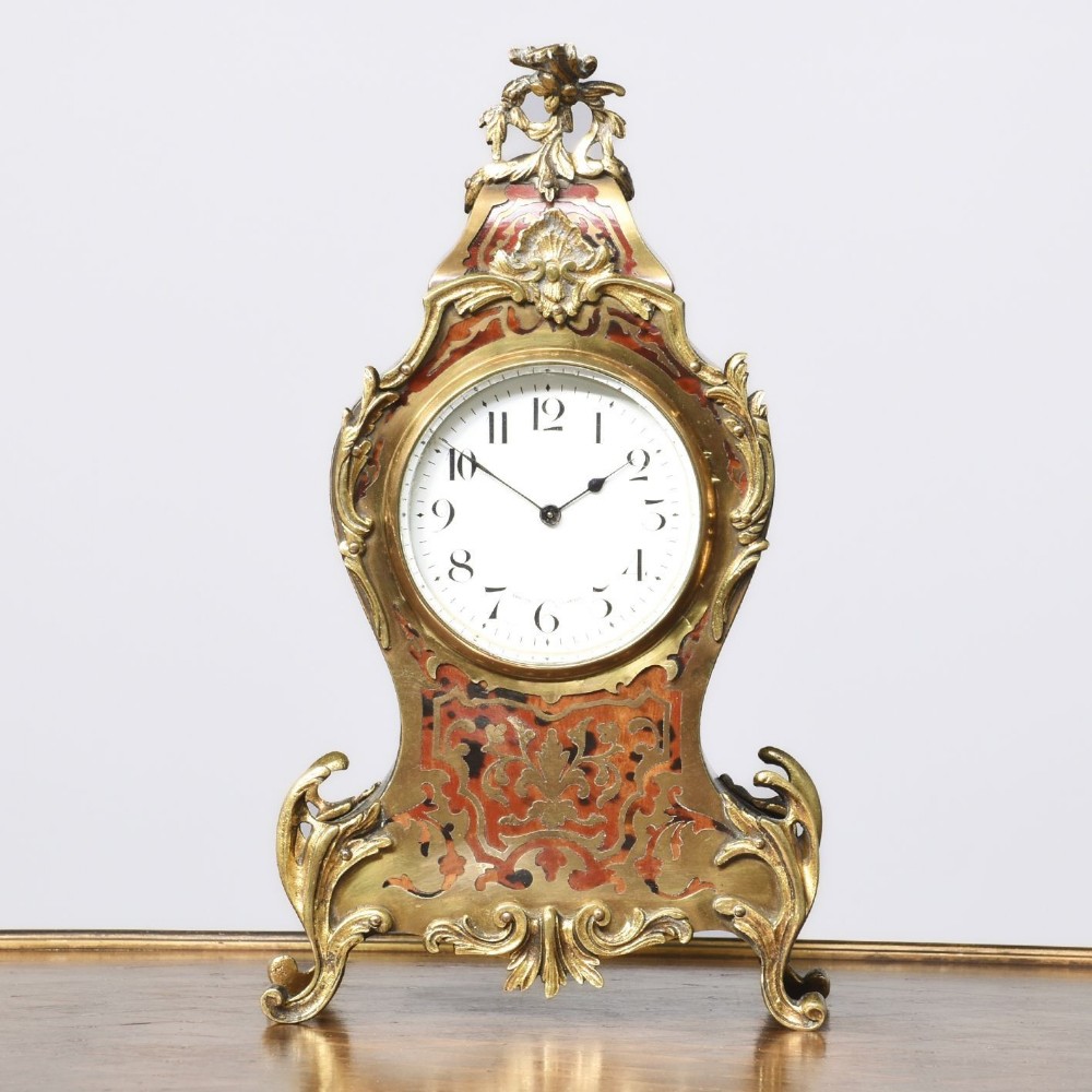 A French Louis XV style Boulle mantel clock featuring brass marquetry inlaid in red tortoiseshell with ornate gilded bronze mounts and an enamel dial.