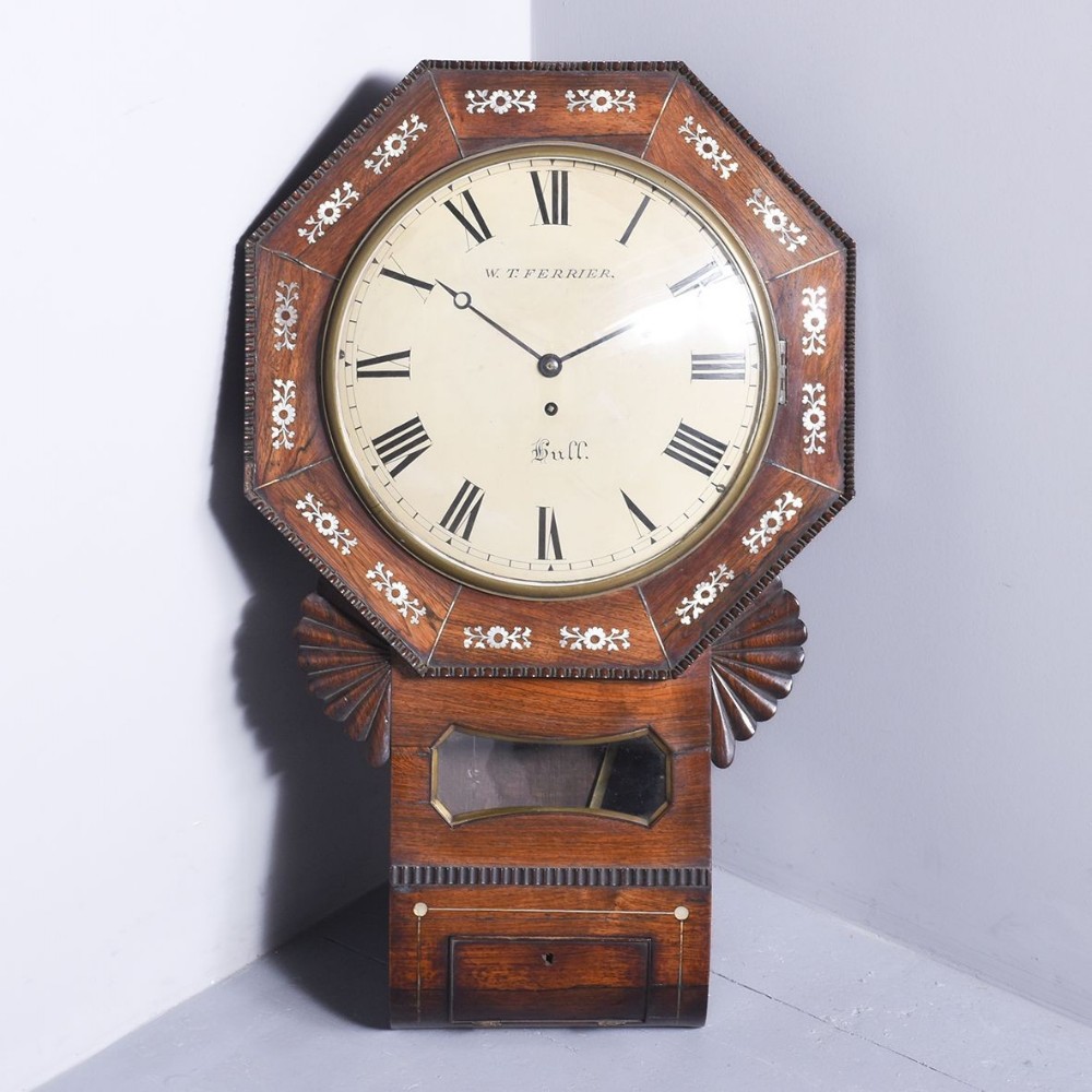 A George IV octagonal rosewood drop dial wall clock featuring mother-of-pearl floral inlays, carved side ears, a cream face with Roman numerals, and a lower pendulum viewing window.