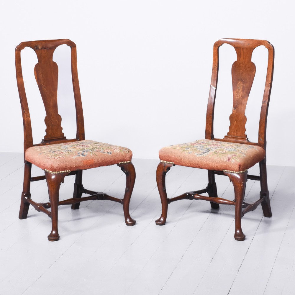 A pair of George II mahogany side chairs featuring vase-shaped splats, floral tapestry seats with brass stud trim, and cabriole front legs ending in pad feet.