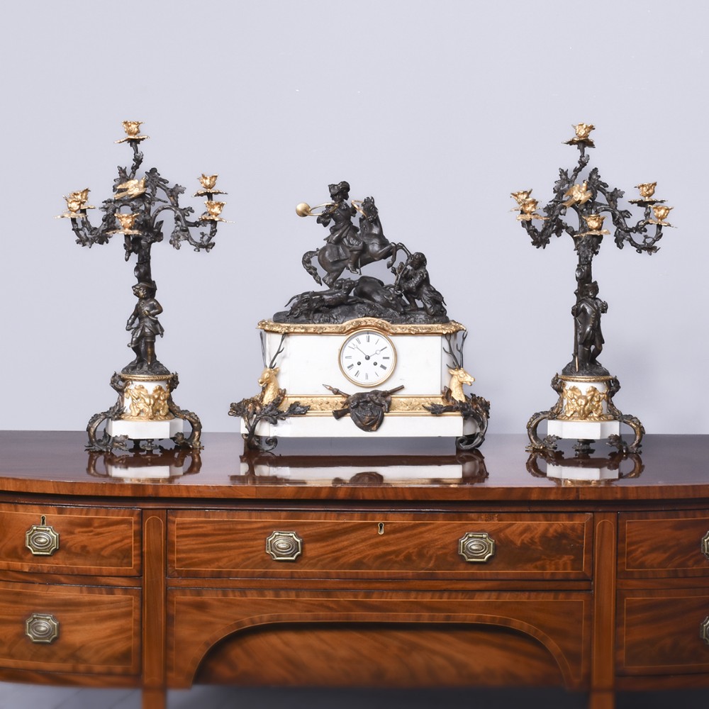A three-piece French Napoleon III clock garniture featuring a central white marble clock topped with a bronze equestrian hunting sculpture, flanked by a pair of matching bronzed and gilt candelabra.