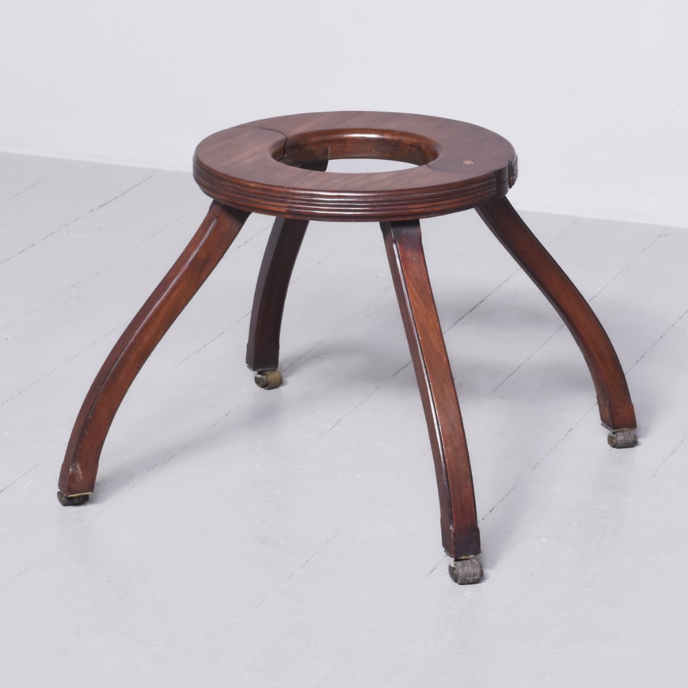 An antique Edwardian dark mahogany childs walker featuring a circular top ring above four splayed curved legs with brass castors.