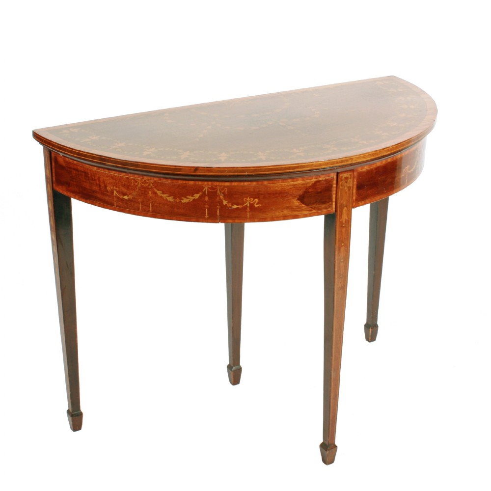 A semi-circular mahogany card table featuring floral marquetry inlay on the top and apron, supported by four square tapered legs.