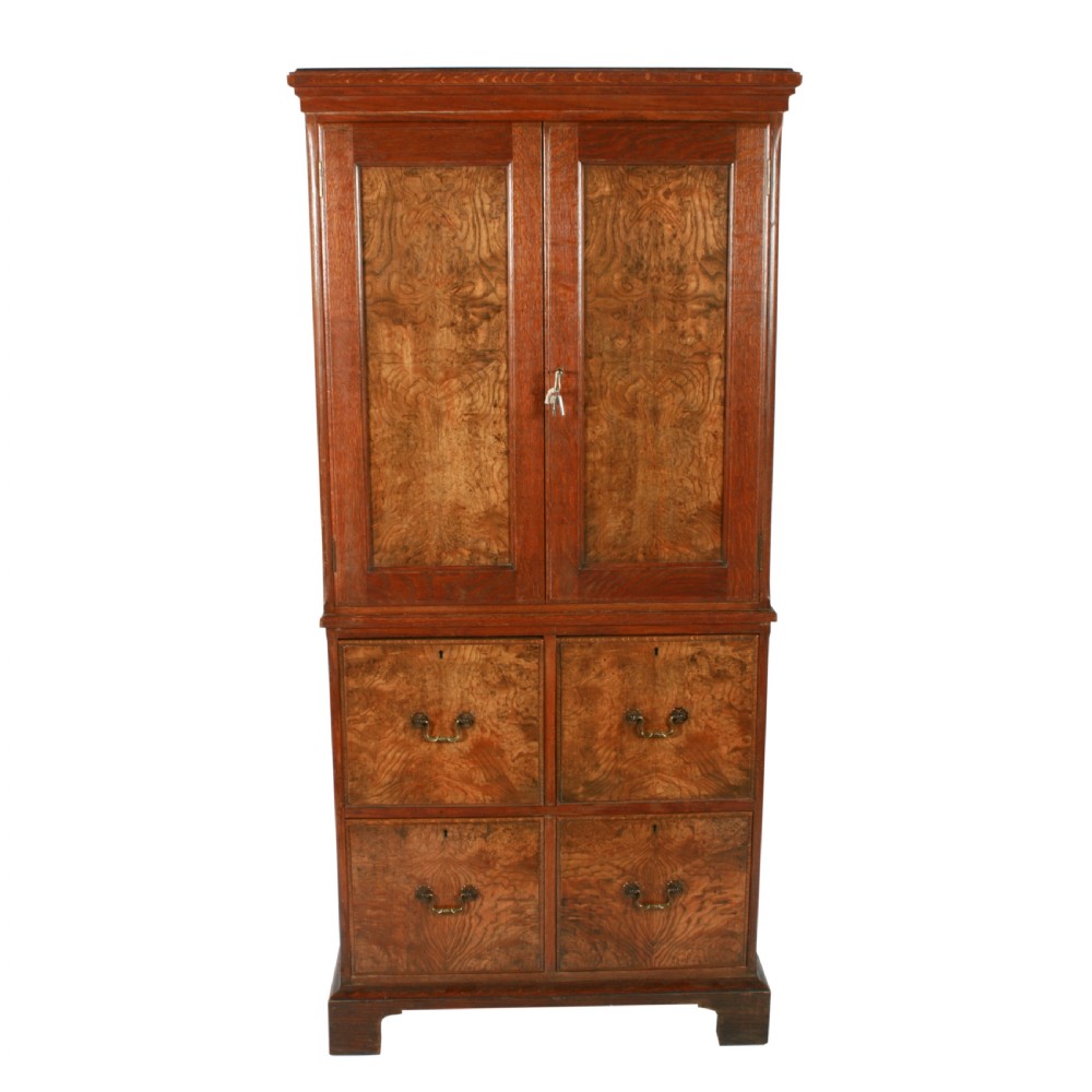 A tall two-section wooden cabinet featuring upper panelled doors with figured veneer and four lower drawers with brass handles. View III