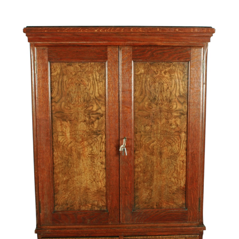 A tall two-section wooden cabinet featuring upper panelled doors with figured veneer and four lower drawers with brass handles. View IV