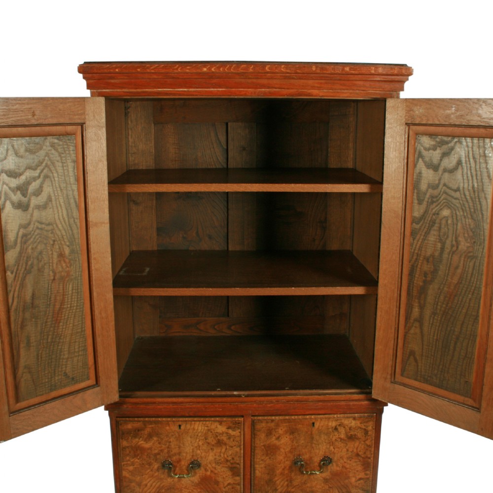 A tall two-section wooden cabinet featuring upper panelled doors with figured veneer and four lower drawers with brass handles. View V