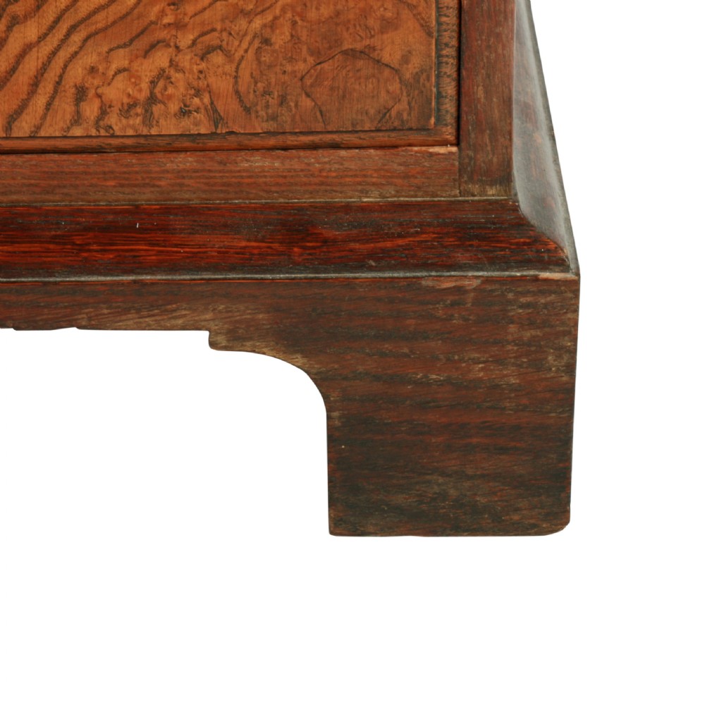 A tall two-section wooden cabinet featuring upper panelled doors with figured veneer and four lower drawers with brass handles. View VII