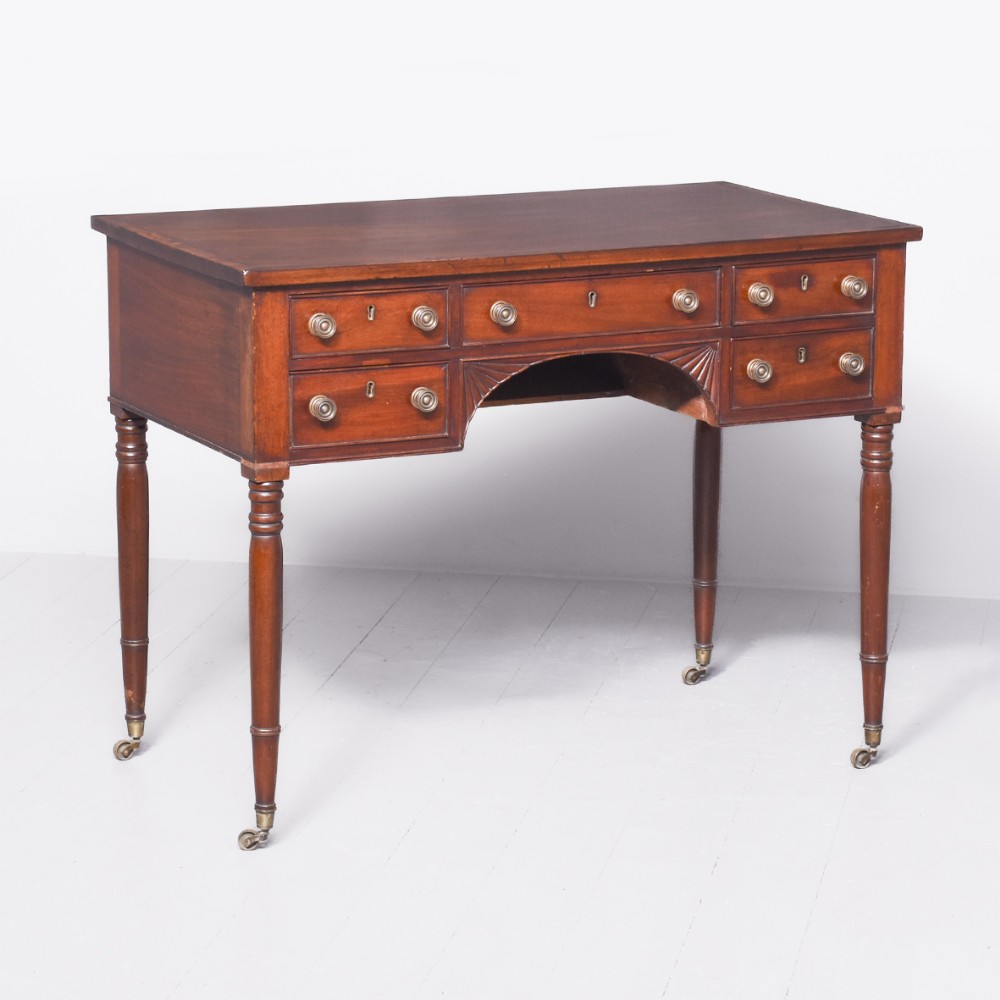 An Irish George III mahogany side table with five drawers, brass knobs, carved fan spandrels, and turned legs on brass castors.