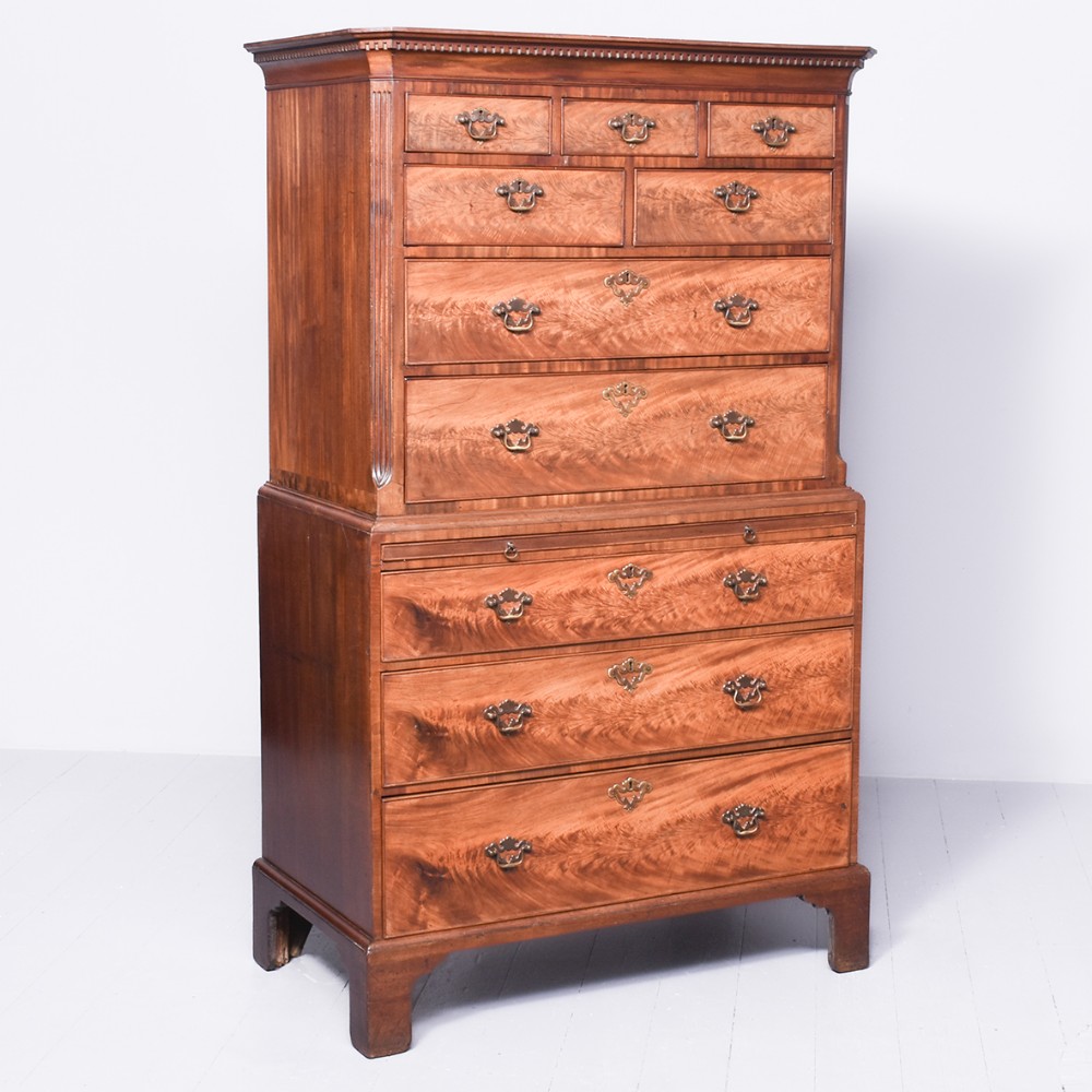 A George III mahogany chest on chest featuring figured flame veneer drawers, brass handles, and bracket feet.