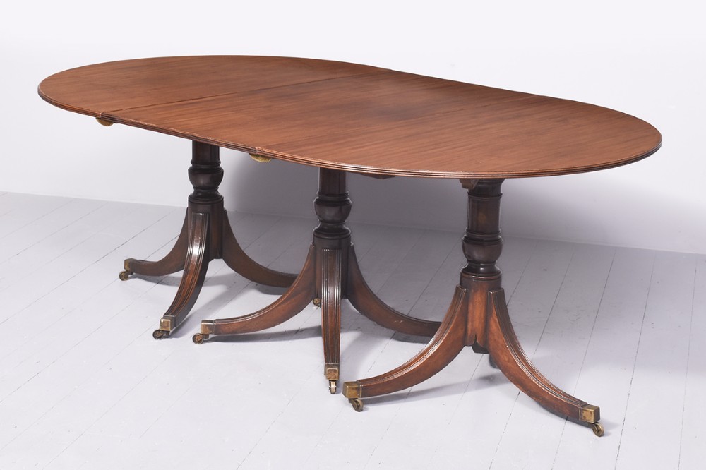 A long George III style mahogany extending dining table supported on three turned pedestal bases with reeded tripod legs and brass castors.