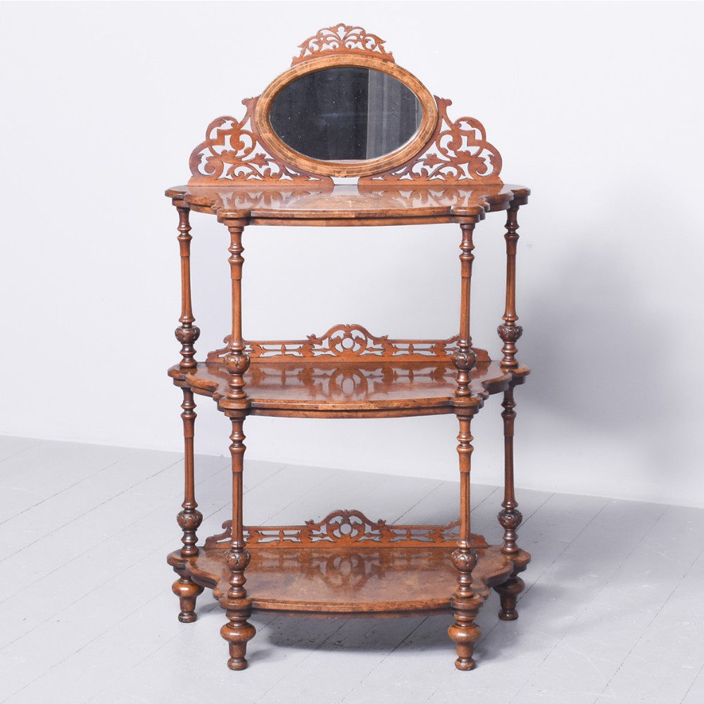 A Victorian burr walnut three-tier whatnot featuring turned supports, pierced fretwork galleries, marquetry inlay, and an oval mirror top.