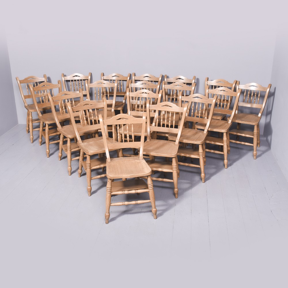 A large set of twenty-two light brown scumbled wood country dining chairs featuring turned spindles, shaped top rails, and solid wooden seats.