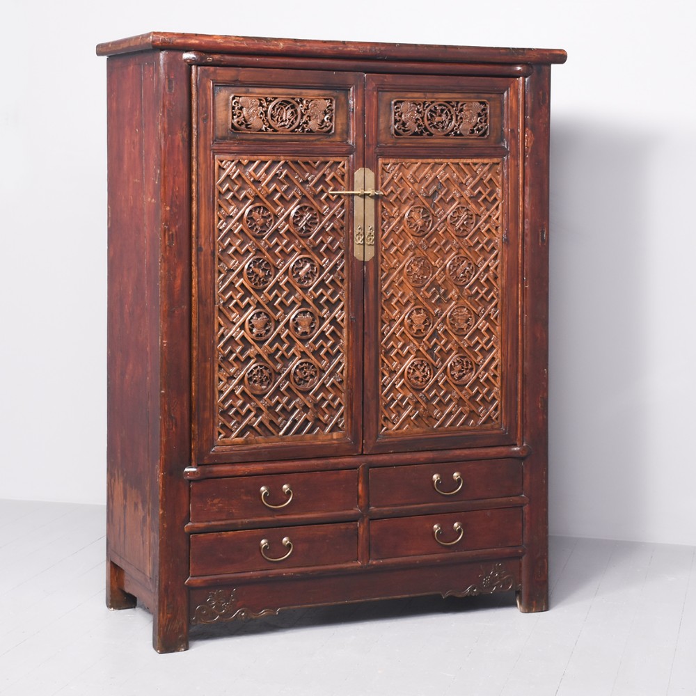 A 19th-century carved hardwood Chinese cupboard with geometric lattice panel doors, brass hardware, and four lower drawers.