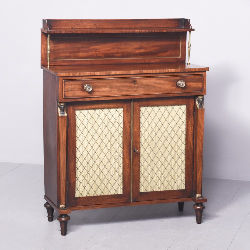A Regency mahogany chiffonier with a top drawer, brass wire lattice cupboard doors backed with fabric, and a raised upper shelf supported by brass columns.
