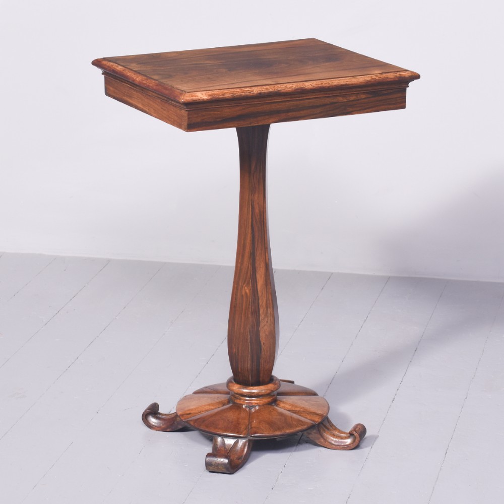 A rectangular rosewood lamp table featuring a central faceted pedestal and a shaped quadform platform base with scroll feet.