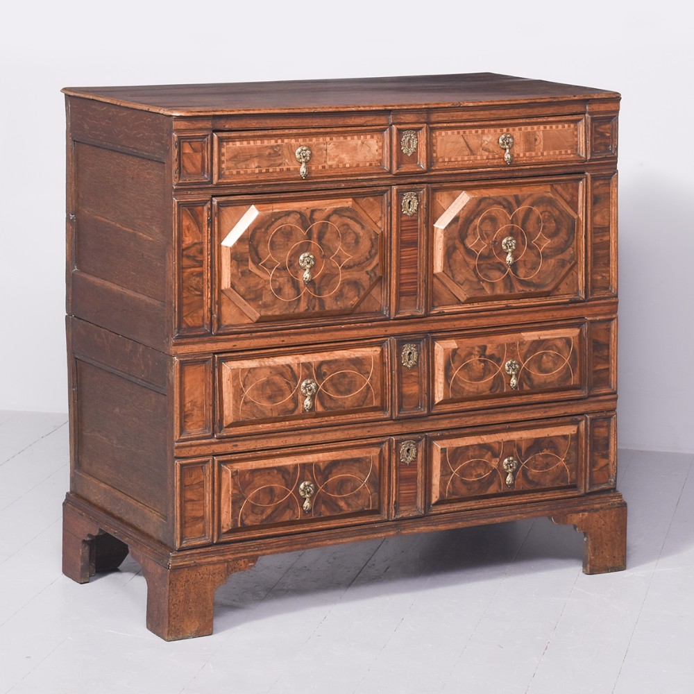 A Charles II period two-part oak chest of drawers decorated with geometric walnut marquetry panels and brass teardrop drop handles.