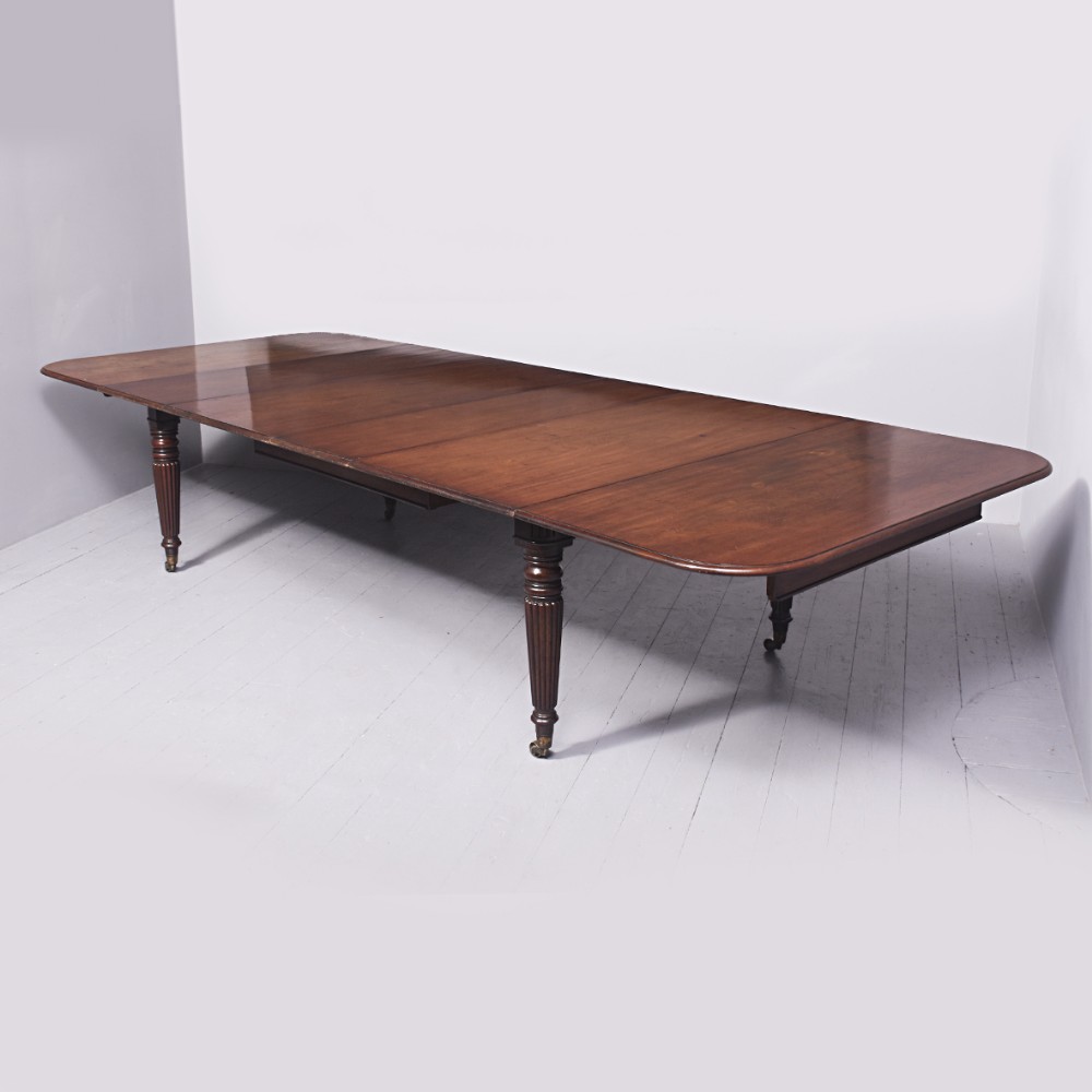 A large extendable mahogany dining table featuring reeded turned legs set on brass castors with a polished surface.