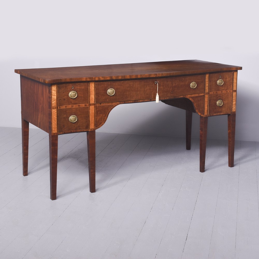 A George III mahogany sideboard featuring string inlay, brass ring handles, an arched central recess, and tapered square legs.